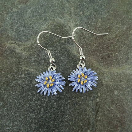 A pair of handmade dangle earrings featuring small blue and yellow flower charms on silver fishhook wires, displayed on a dark textured slate surface.