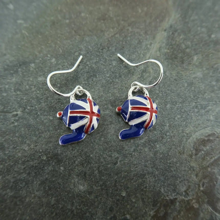 A pair of silver fishhook earrings with small enamel hat charms decorated in a Union Jack pattern, resting on a dark gray slate surface.