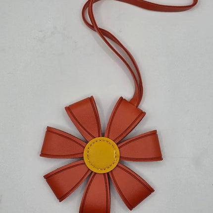 A flower-shaped crossbody bag with reddish-brown petal-like sections, a yellow center, and a matching reddish-brown strap, shown on a light gray background.