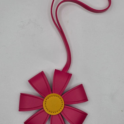A flower-shaped handbag or pouch in vibrant magenta pink faux leather with a yellow circular center and a matching pink strap, shown on a light gray background.