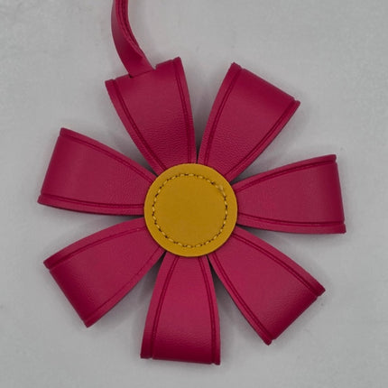 A flower-shaped leather bag charm or ornament in vibrant magenta pink with a contrasting yellow center, shown on a light gray background.