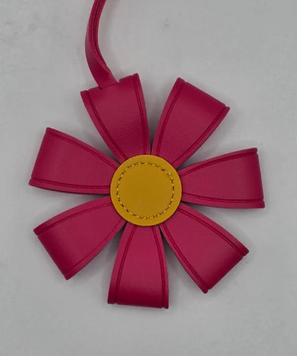 A flower-shaped leather bag charm or ornament in vibrant magenta pink with a contrasting yellow center, shown on a light gray background.