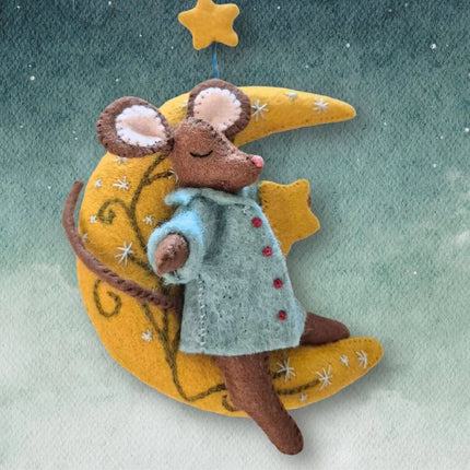 A felt mouse wearing a light blue coat with red buttons, resting on a yellow crescent moon and star decoration against a soft green-blue textured background.