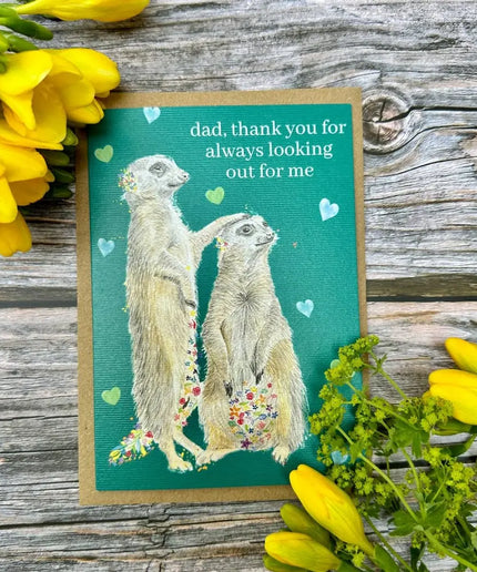 Greeting card with meerkats and flowers on a wooden surface