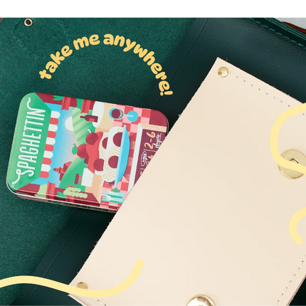 A close-up of a dark green leather wallet or clutch with a cream-colored snap flap, showing a small colorful 'Spaghetti' card tucked inside. Yellow decorative script text reads 'take me anywhere!' and wavy lines overlay the photo.